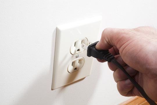 A hand putting a two prong plug into a wall socket.