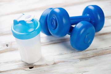 Protein shake and plastic dumbbells on a wooden surface