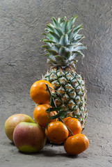 Pineapple fruits,apples and orange on a gray background