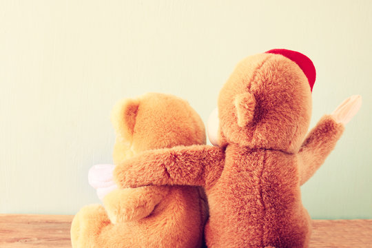 two teddy bears on a shelf with arms around each other