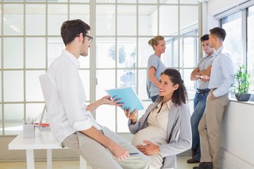 Obraz premium Pregnant businesswoman talking with colleague sitting at desk
