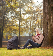 Obraz premium Blond girl texting by phone seated in park