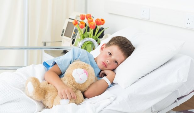 Boy lying with teddy bear in hospital