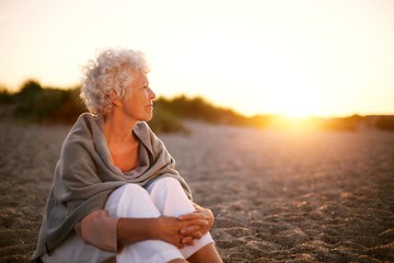 Old woman sitting on the beach looking away at copyspace - Powered by Adobe
