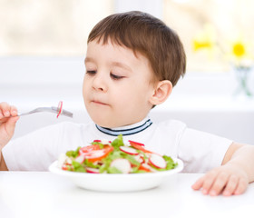 Cute little boy is eating vegetable salad