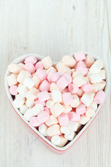 marshmallows in heart shape bowl on a wooden table