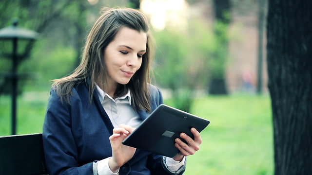 Young businesswoman with tablet computer sitting on bench in par