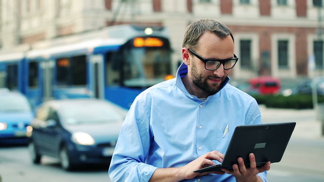 Young man with modern laptop standing by the city street
