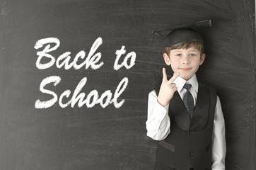 Cheerful little boy on blackboard. Looking at camera