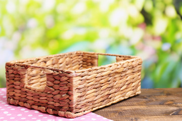 Empty wicker basket on wooden table, on bright background