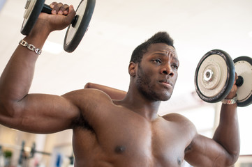 Strong black man exercising with dumbbells in the gym.