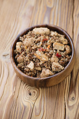 Bowl with stewed buckwheat and chicken fillet, wooden background