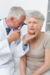 Male doctor examining senior patient's ear