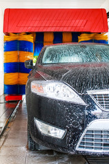 Black car in automatic car wash, rotating blue and yellow brushe