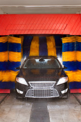 Black car in automatic car wash, rotating blue and yellow brushe