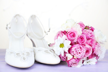 Beautiful wedding bouquet and shoes on table on light