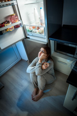 woman sitting on floor and looking at fridge at night