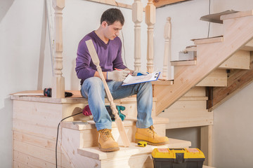 young handsome man sitting on floor holding clipboard with bluep