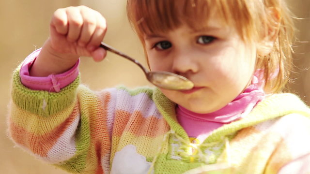 Outdoor portrait : Cute Little girl eats with spoon