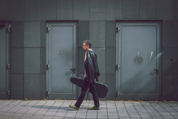 Man in short sleeve shirt walking with guitar case - obrazy, fototapety, plakaty