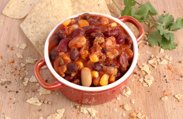 Chili con carne in red bowl with nacho chips and spice