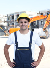 Stehender Bauarbeiter mit rotem Bagger im Hintergrund