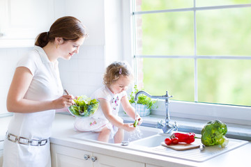 Young mother and her adorable toddler daughter cooking salad