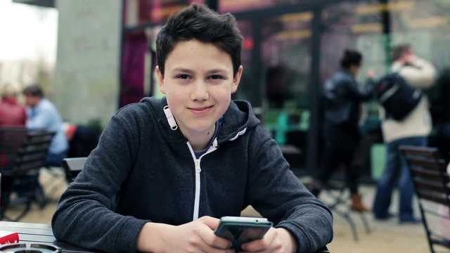 Happy young teenager with smartphone sitting in cafe