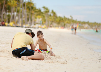 Caucasian boy and father playing with sand at tropical beach