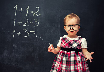 baby girl  in glasses and chalk at a school board with arithmeti