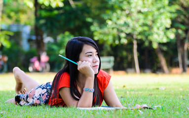 A pretty young woman writing down notes while lying on the grass
