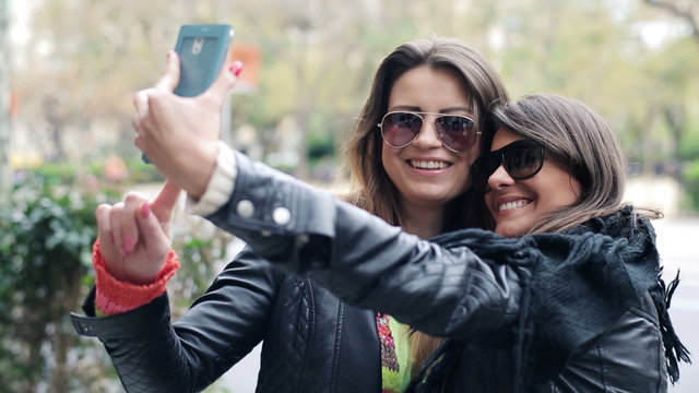 Two happy girlfriends taking photo with their smartphone