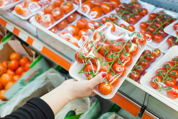 Packaged tomato with woman hand in the supermarket - obrazy, fototapety, plakaty