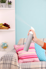 Sprayed air freshener in hand on home interior background