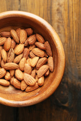 Almonds in bowl on color wooden background