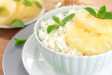 Bowl of tasty cottage cheese with pineapple on wooden table