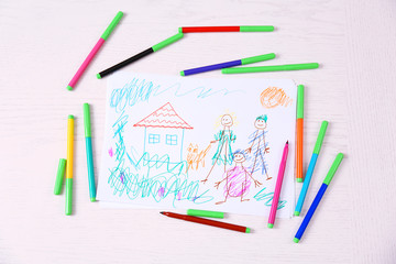 Kids drawing of family and colored pencils on wooden table