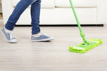 Woman with mop cleaning wooden floor from dust