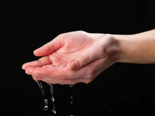 Human hands with water splashing on them on black background