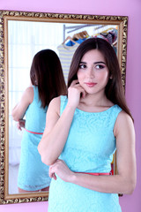 Beautiful girl trying dress near mirror in room