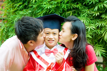 Asian parent kiss their son on his kinder graduation day.