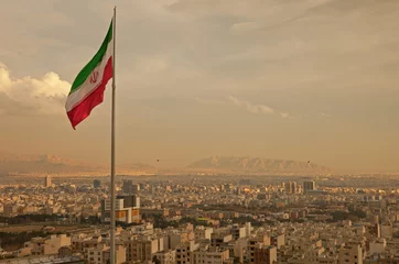 Selbstklebende Fototapeten Iran Flag in the Wind Above Skyline of Tehran © Borna_Mir