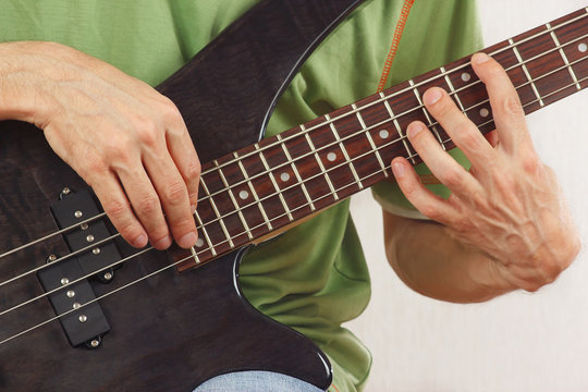 Hands of man playing the electric bass guitar closeup