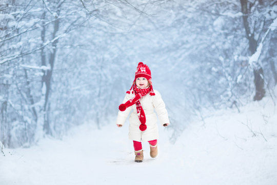 Cute toddler girl in a white jacket and red hat in snowy park