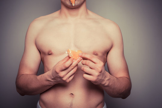 Athletic shirtlss man peeling an orange