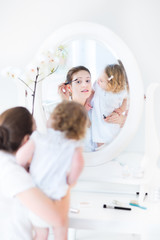 Beautiful young woman applying make up with her toddler daughter