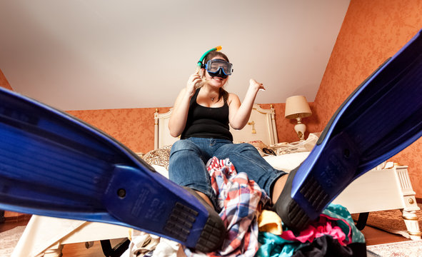 Woman In Flippers And Mask Sitting On Suitcase At Home