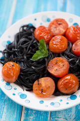 Close-up of black tagliatelle with fried tomatoes, vertical shot