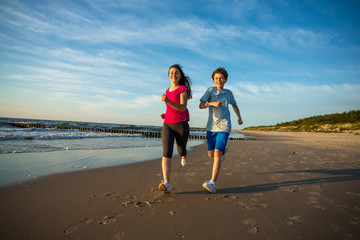 Teenage girl and boy running, jumping on beach