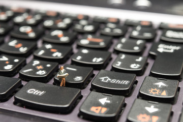 パソコンのキーボードに座って仕事をするミニチュアの人形